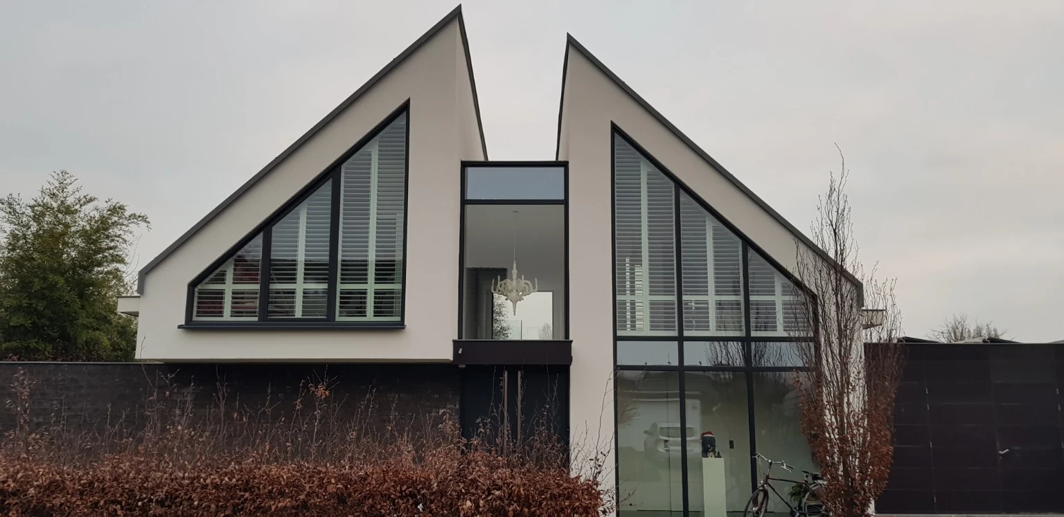 Außenansicht weißer Innenfensterläden an den spitz zulaufenden Fenstern in Haacht, mit 89-mm-Lamellen und ClearView.