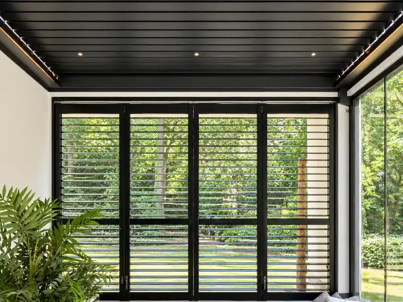 Schwarze Aluminium-Shutters auf Schienen unter einem Lamellendach in Overijse